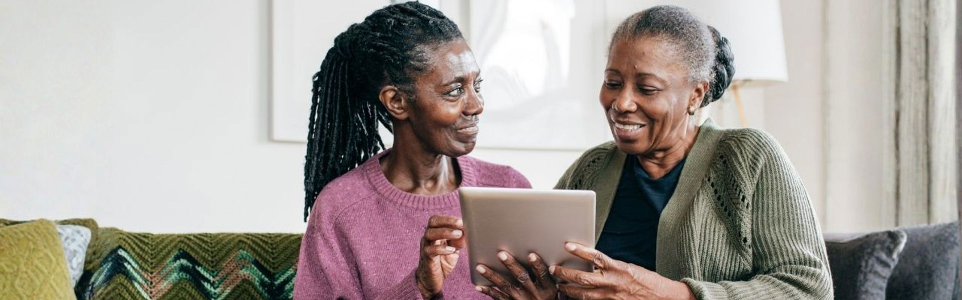 A mother and daughter sat on the sofa together looking through dementia resources on a tablet together.