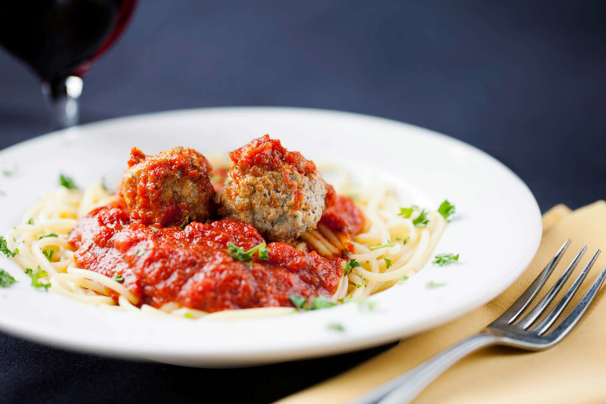 spaghetti and meatballs in a white pasta bowl garnished with green herbs