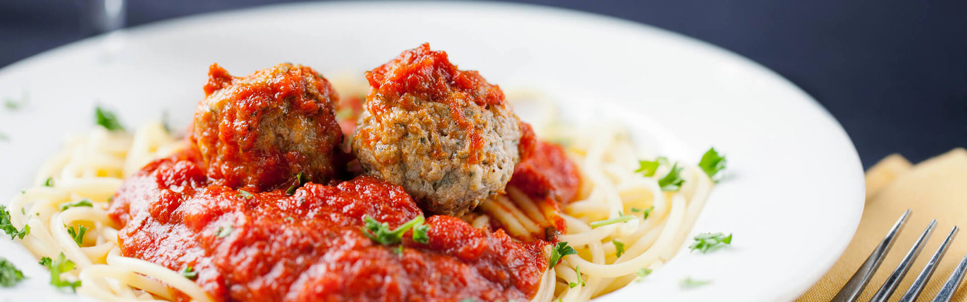 spaghetti and meatballs in a white pasta bowl garnished with green herbs