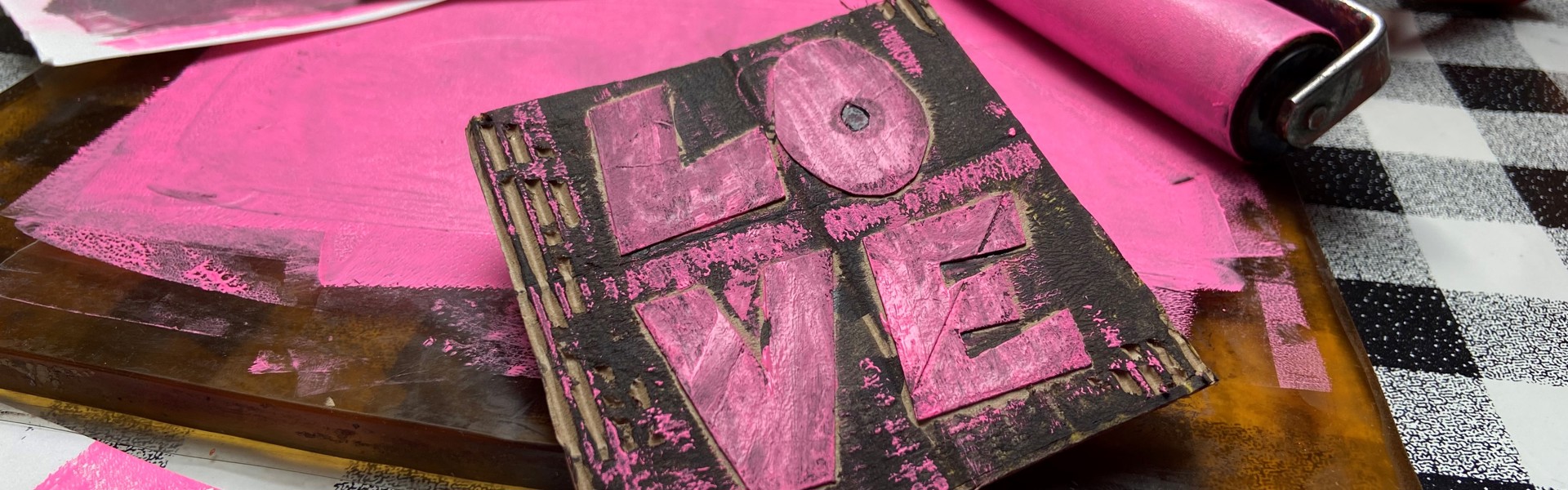 A close up of a printing block with the word 'LOVE' engraved into it covered in pink paint