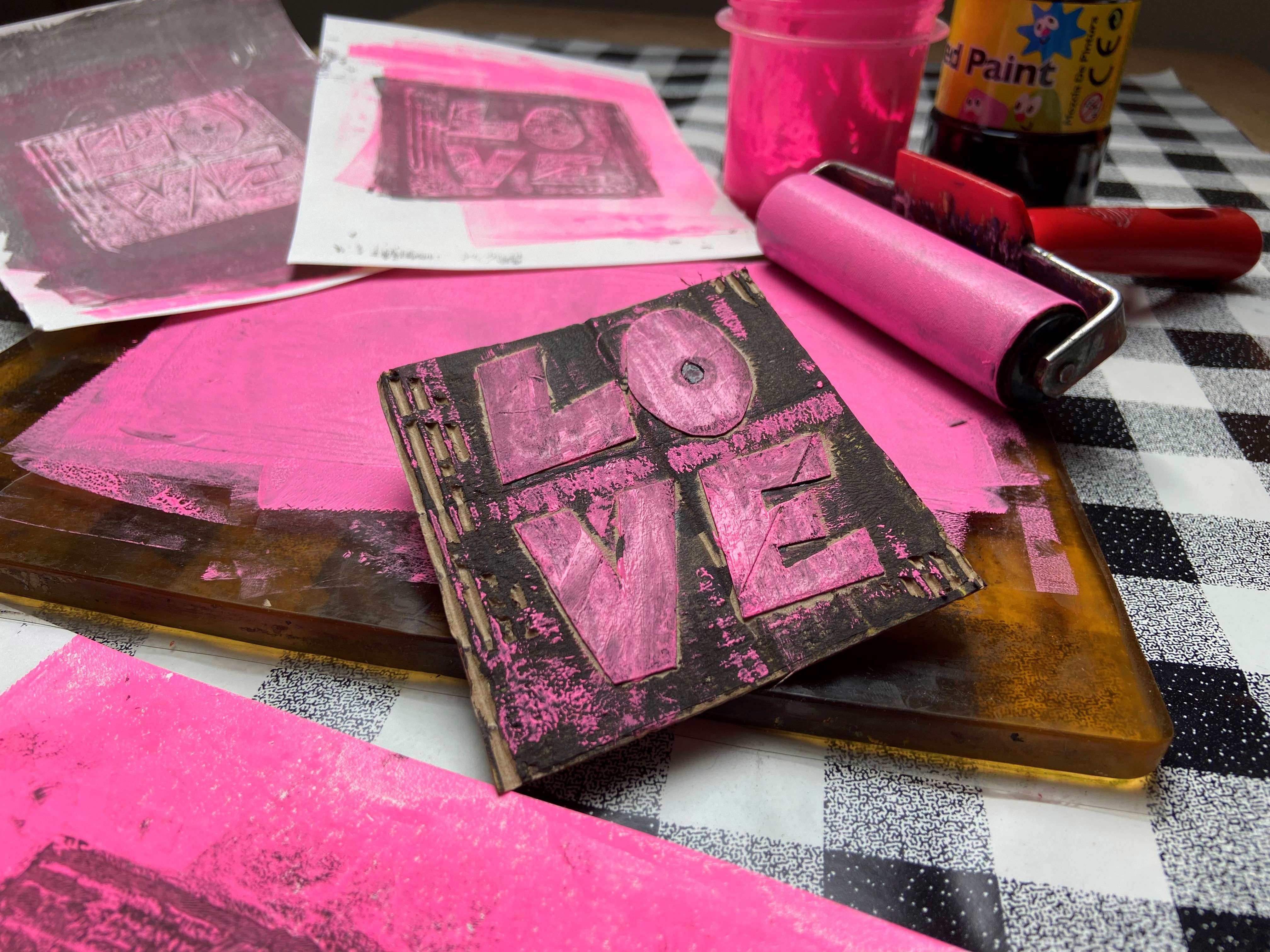 A close up of a printing block with the word 'LOVE' engraved into it covered in pink paint