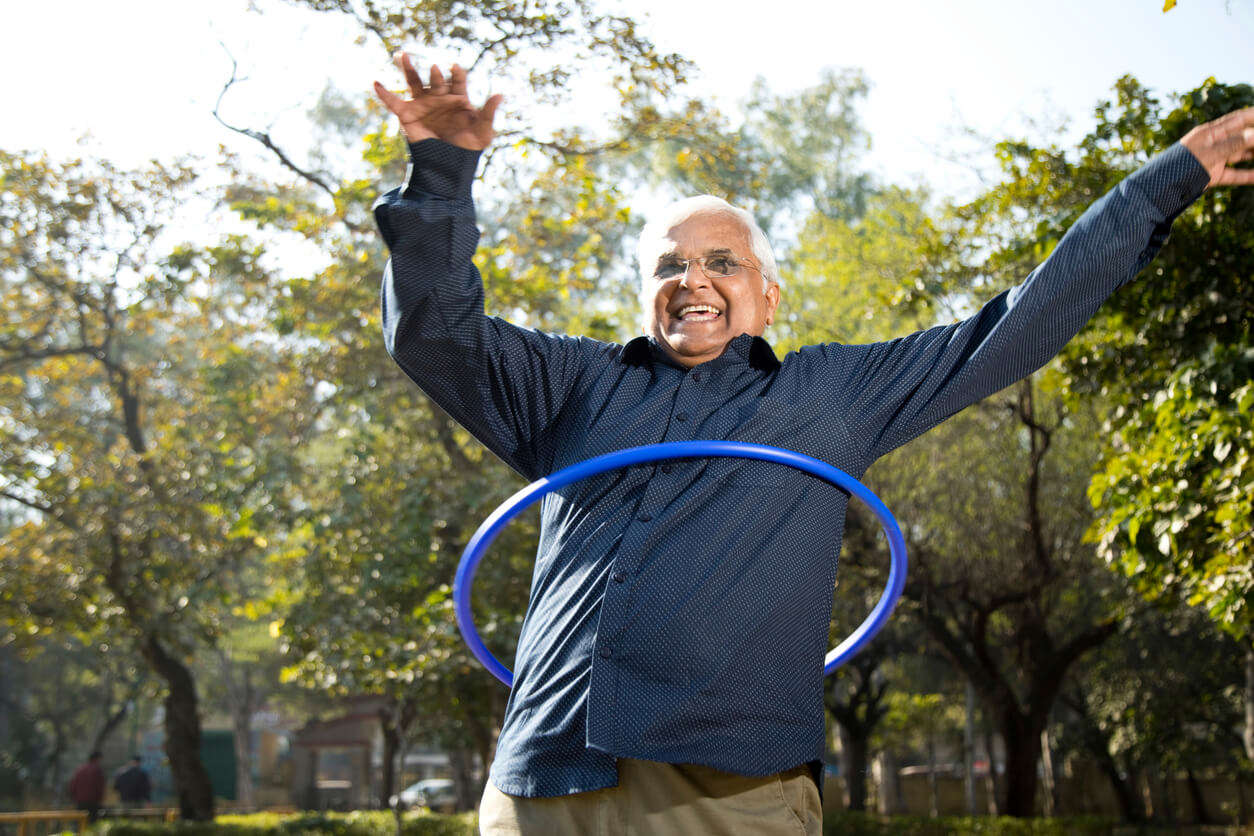 An older man with glasses hula hooping outdoors
