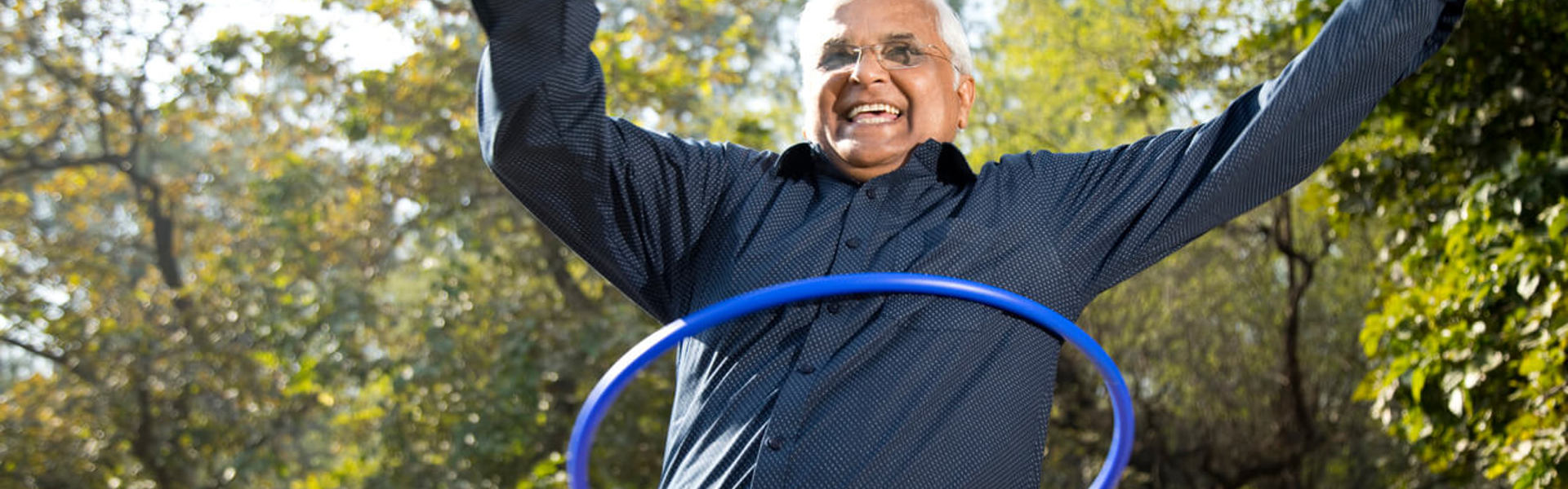 An older man with glasses hula hooping outdoors