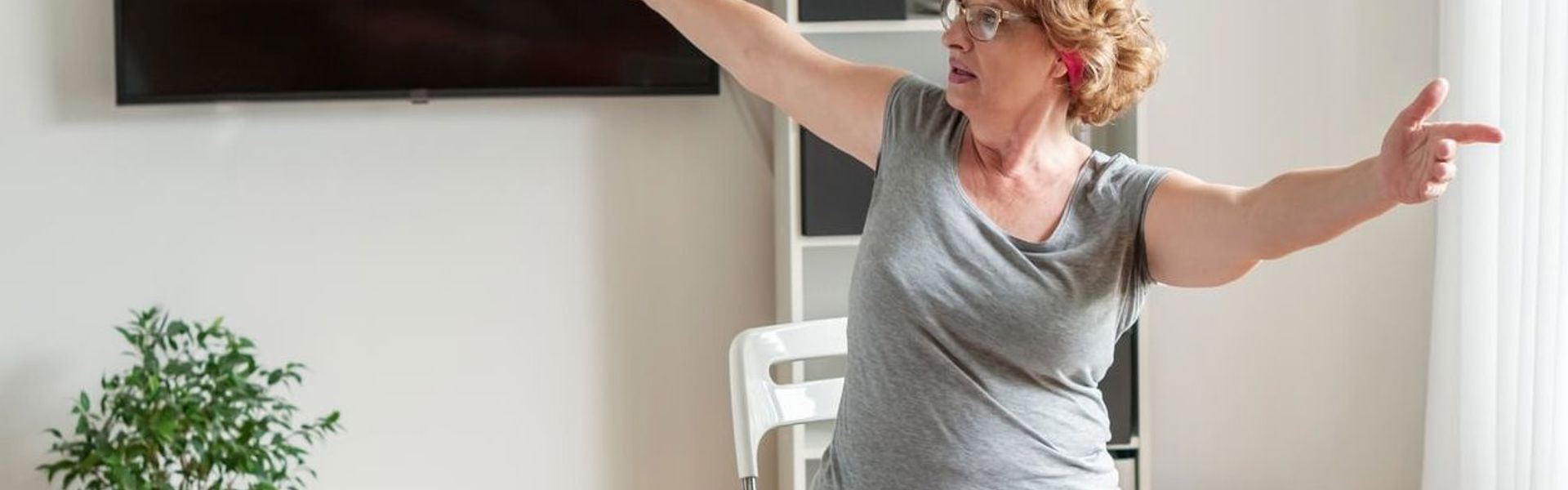 Main Image: Woman sitting in her living room doing chair yoga stretches