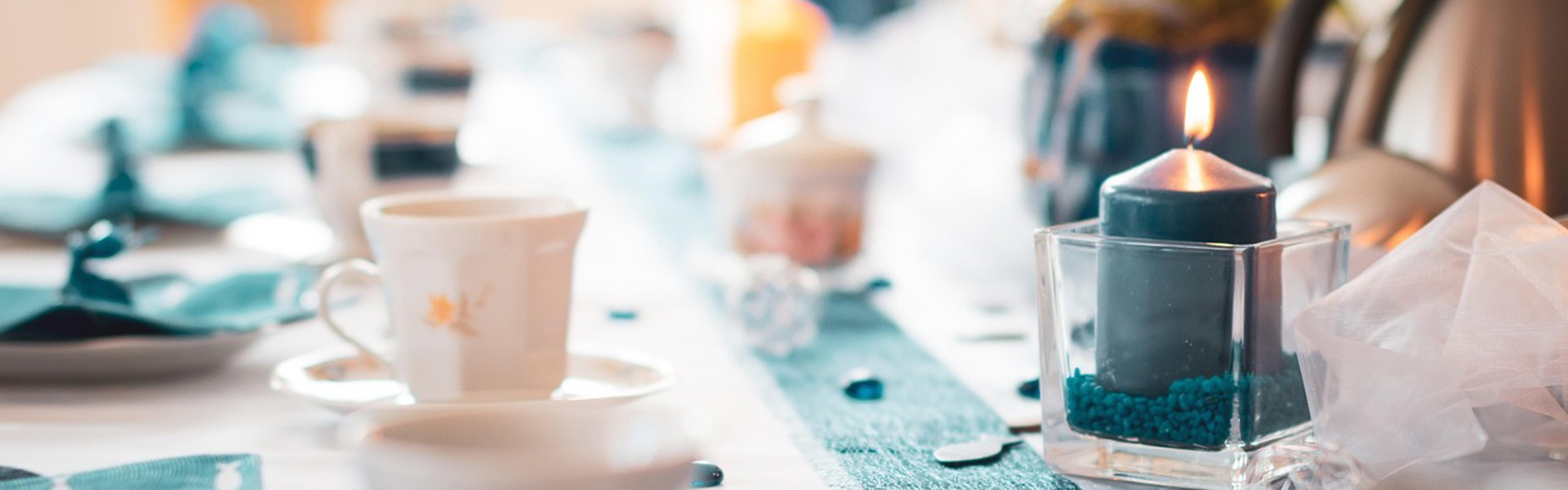Main image: a dinner party table, with tea cups, candles and a DIY hand printed table runner, in teal and white colours.