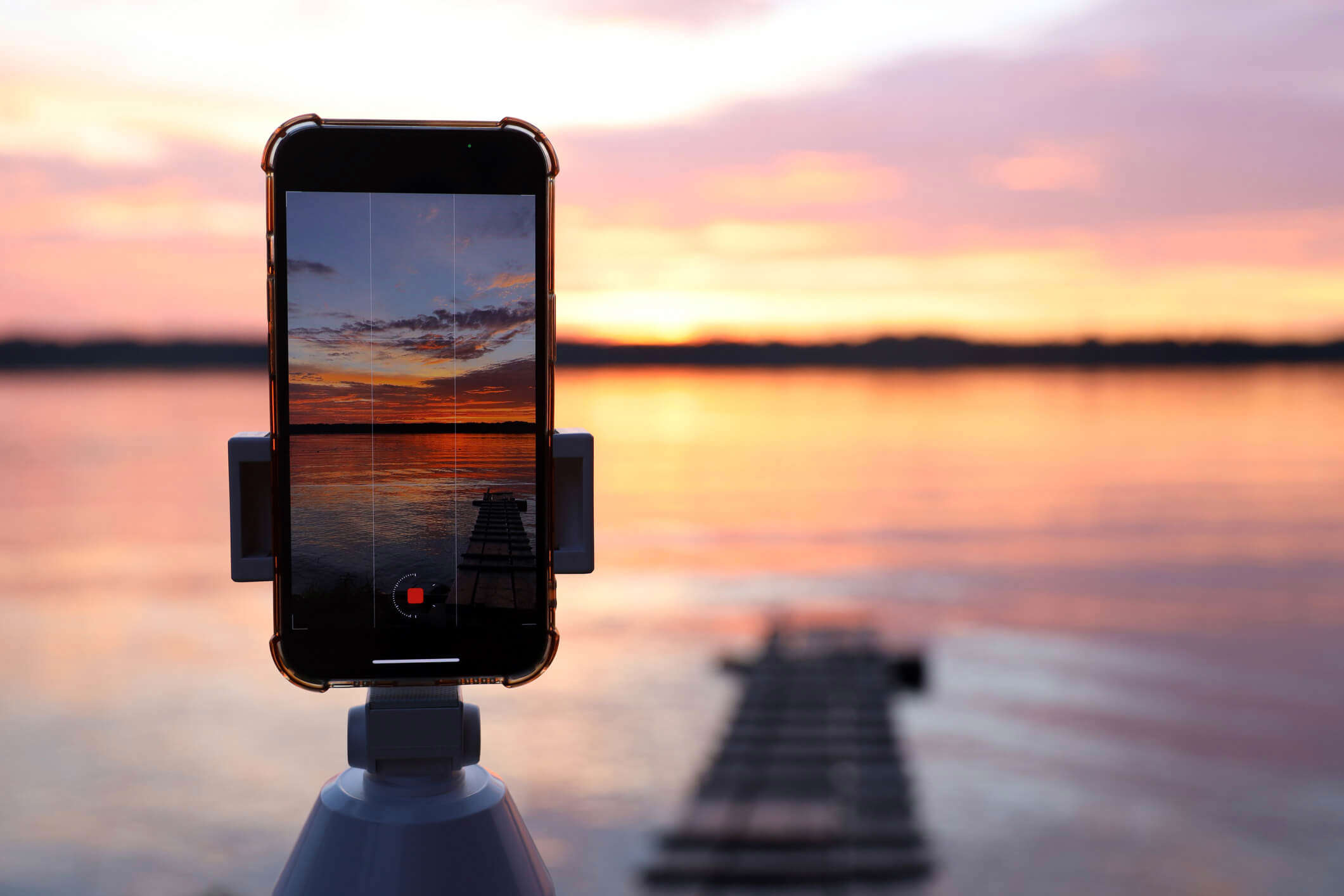 an iphone set up in a tripod capturing a pink and orange sunset horizon