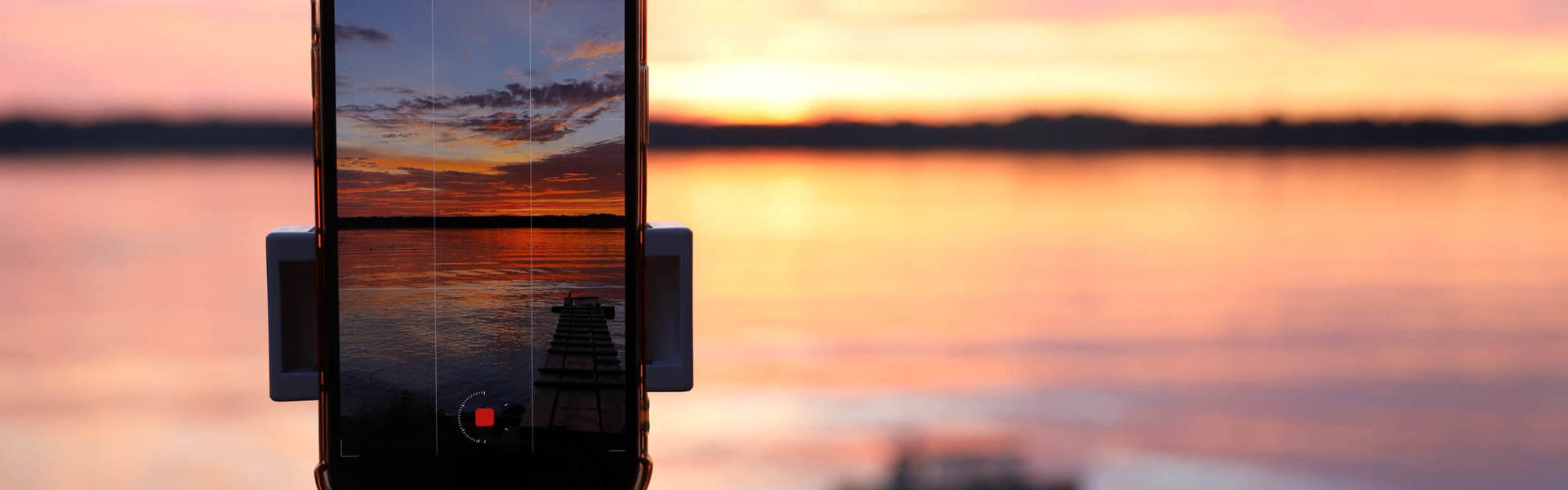 an iphone set up in a tripod capturing a pink and orange sunset horizon