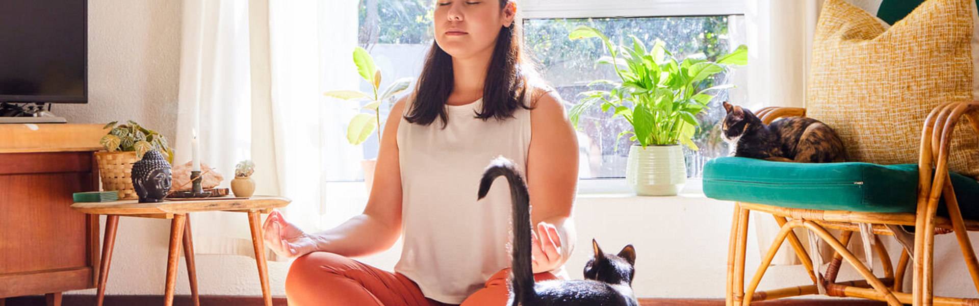 a woman sat cross legged with eyes closed next to a black and white cat in the living room