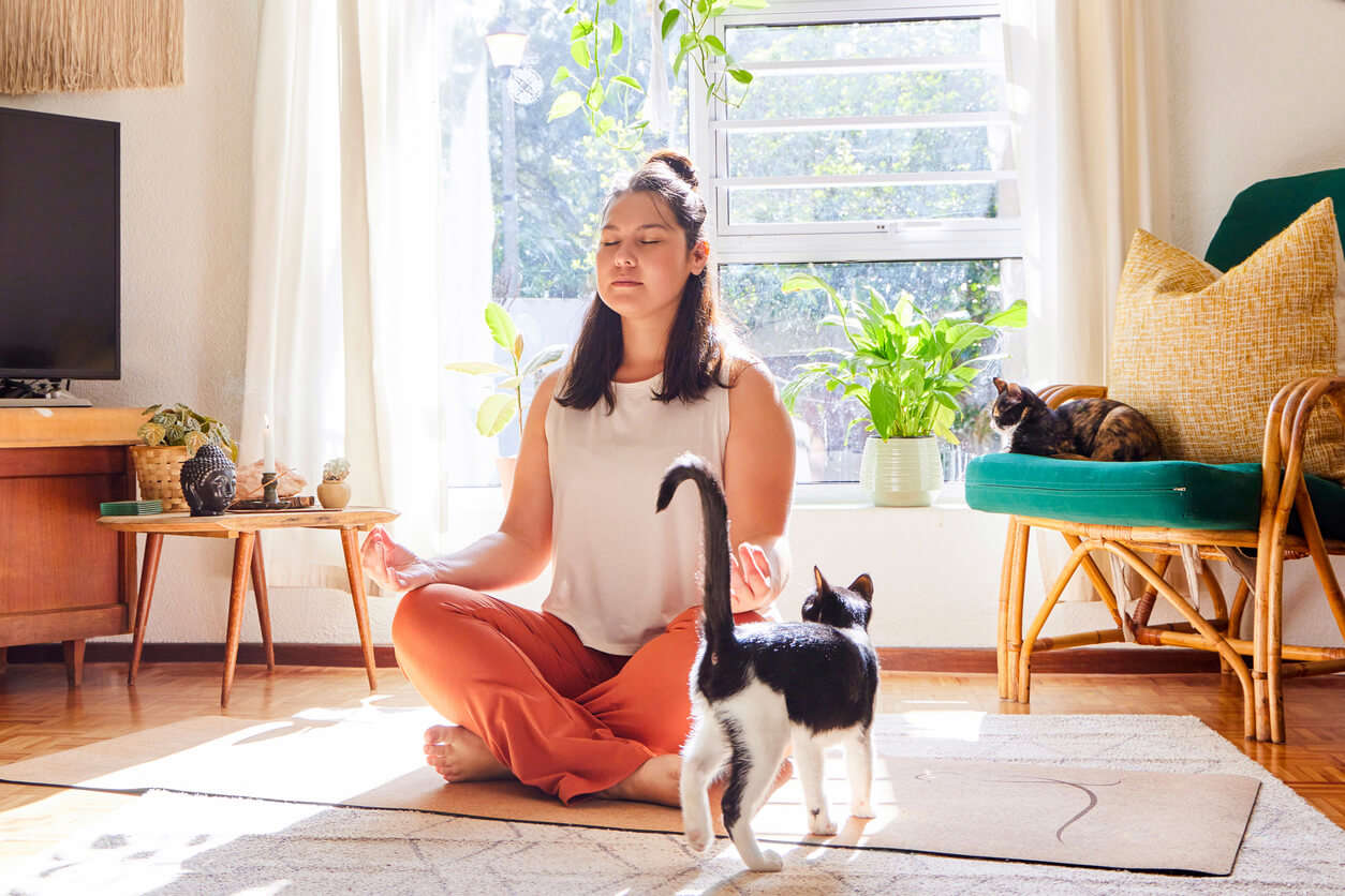 a woman sat cross legged with eyes closed next to a black and white cat in the living room