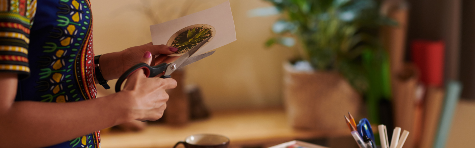 A person making a collage art picture using scissors and scraps of paper and magazines on a wooden table surrounded by art materials