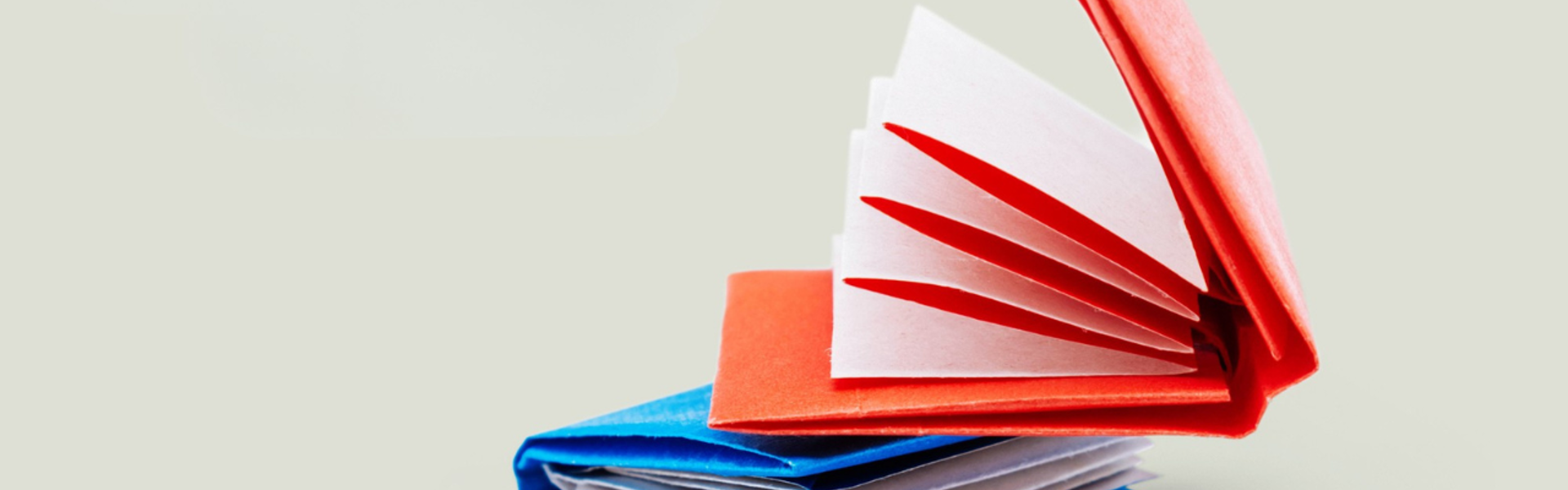 Main image: two mini origami notebooks in red and blue stacked one on top of the other.