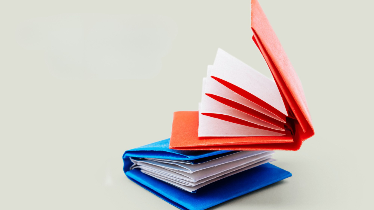 Main image: two mini origami notebooks in red and blue stacked one on top of the other.