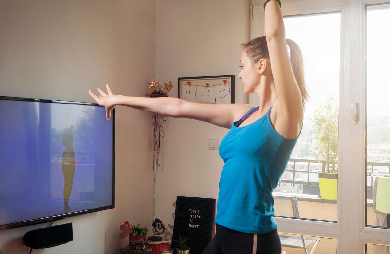 a woman wearing a blue vest dancing in front of the TV