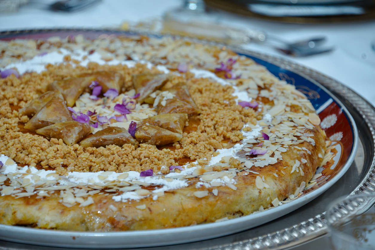 A fish pastilla topped with flaked almonds and edible flowers on a plate