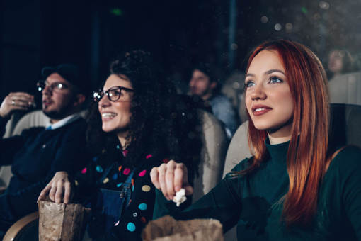 People sat in the cinema watching a film, smiling and eating popcorn.