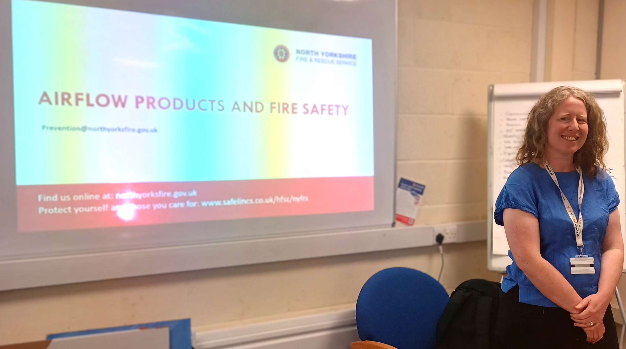 Laura Hodgson prepares to present, standing in front of a large screen displaying her fire safety presentation.