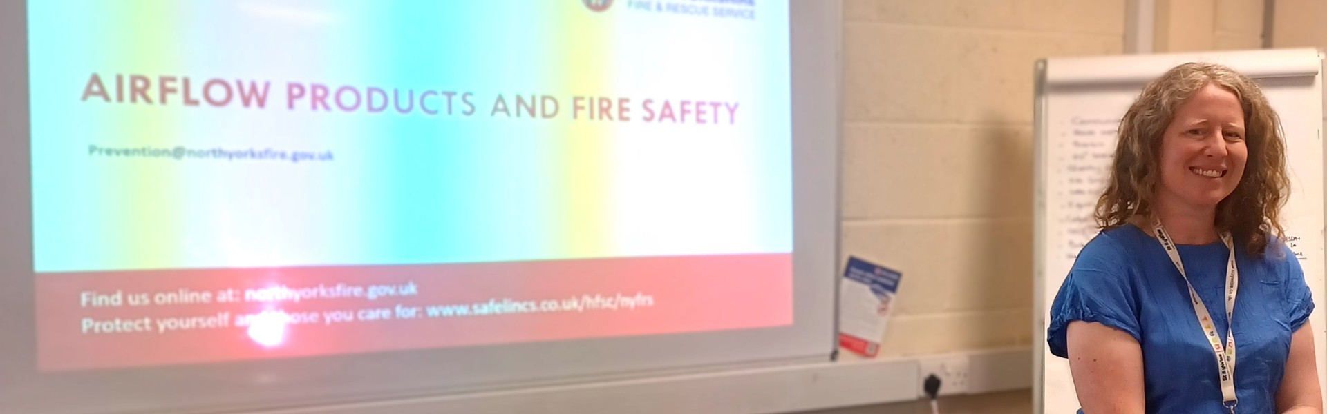 Laura Hodgson prepares to present, standing in front of a large screen displaying her fire safety presentation.