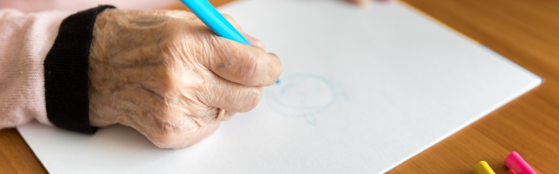 a close up of an older person drawing with a blue colouring pencil