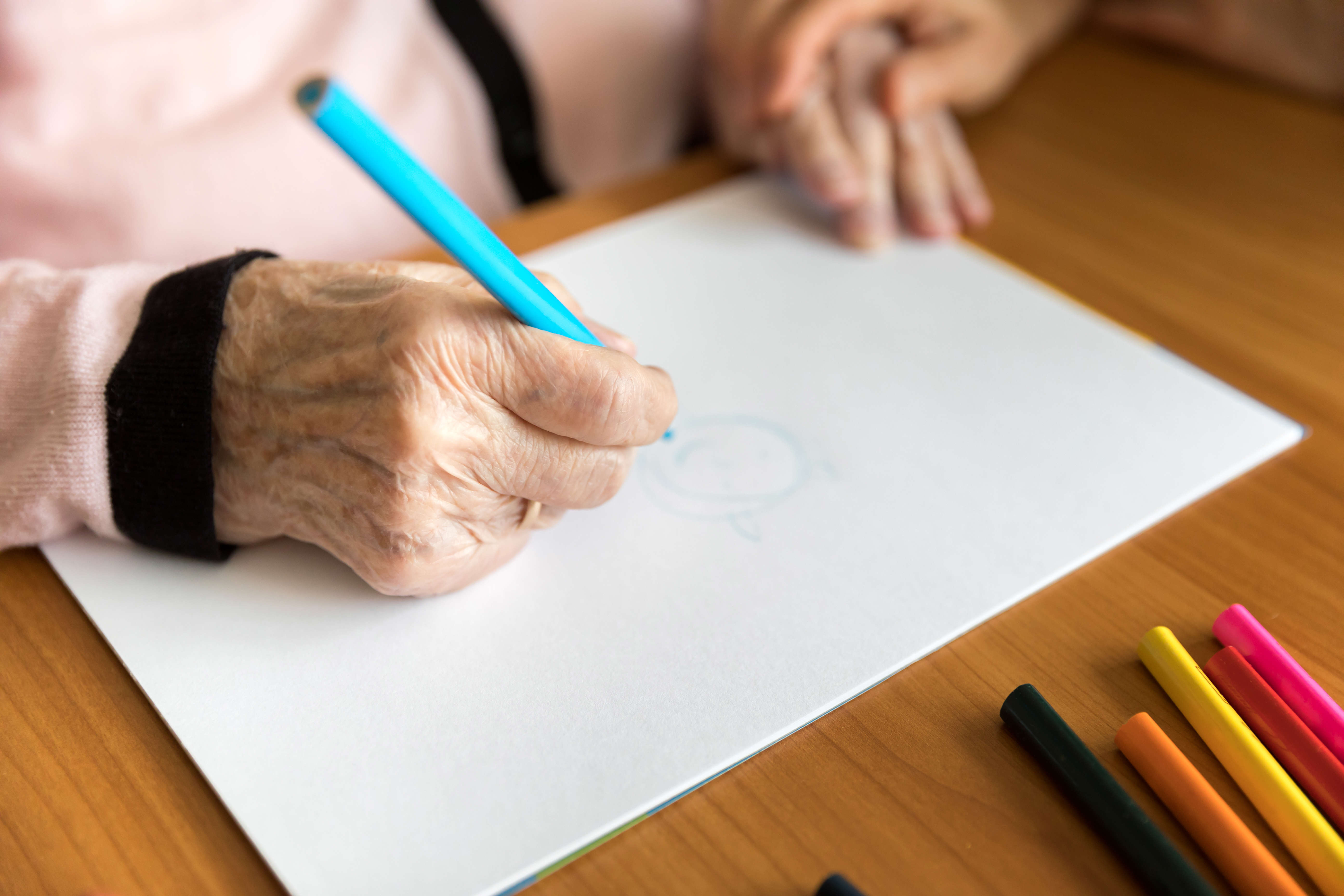 a close up of an older person drawing with a blue colouring pencil