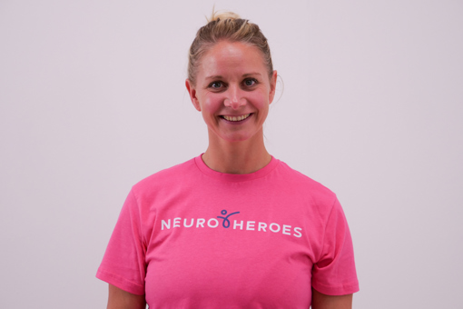 Headshot photo of Anna Kharin, Neurological Physiotherapist from Neuro Heroes, smiling and wearing a bright pink t-shirt that reads "NEURO HEROES" on the front. Against a white backdrop.