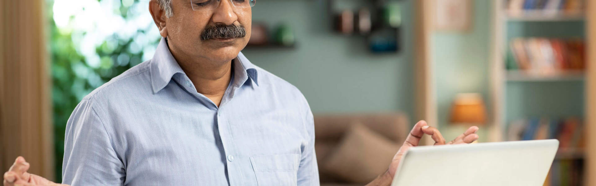 A man sat at a desk with his laptop open meditating