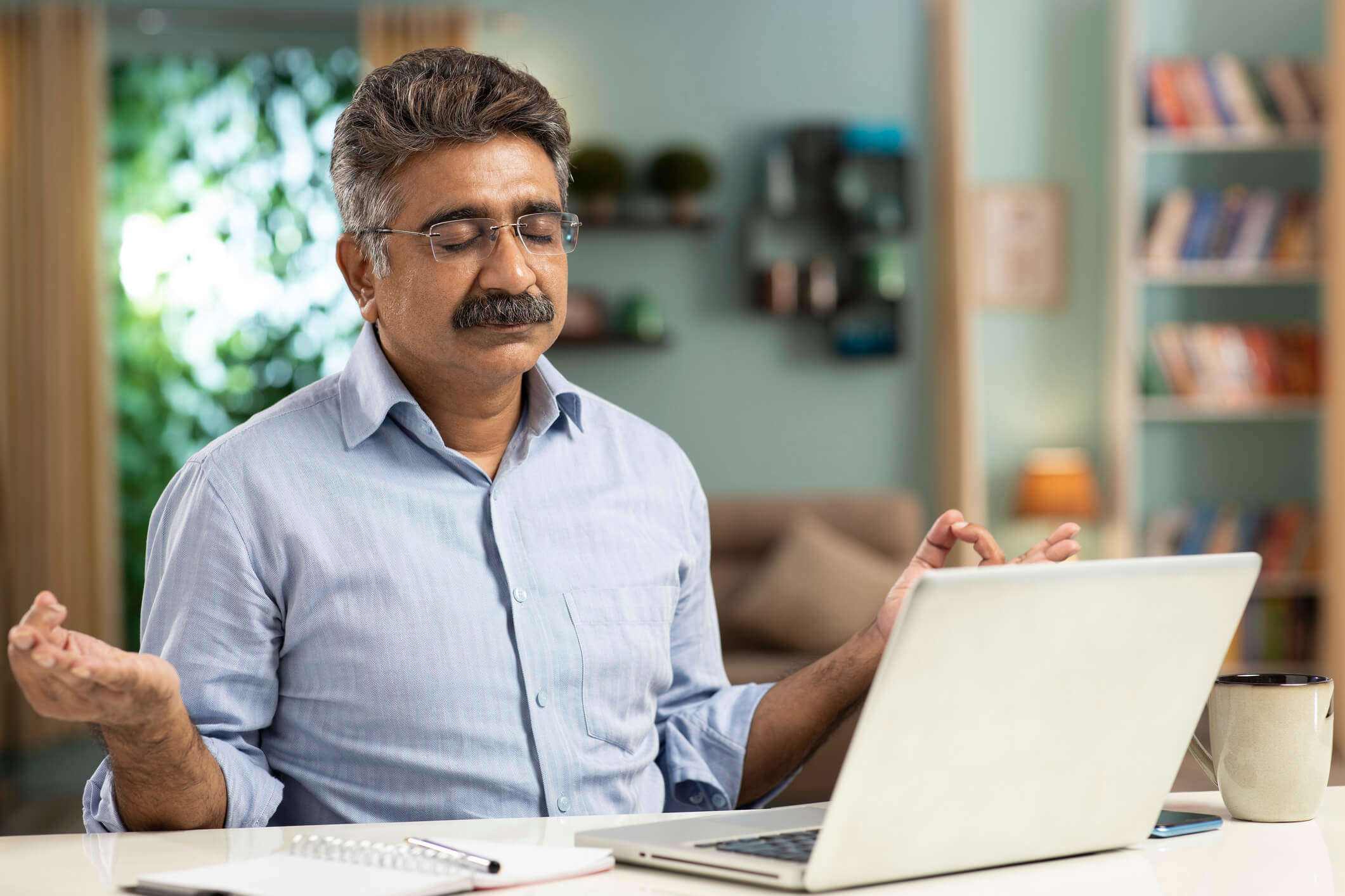 A man sat at a desk with his laptop open meditating