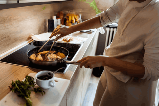 Main Image: A person pan-frying basa fish fillets on the hob, with herbs and cooking accessories on the kitchen counter.