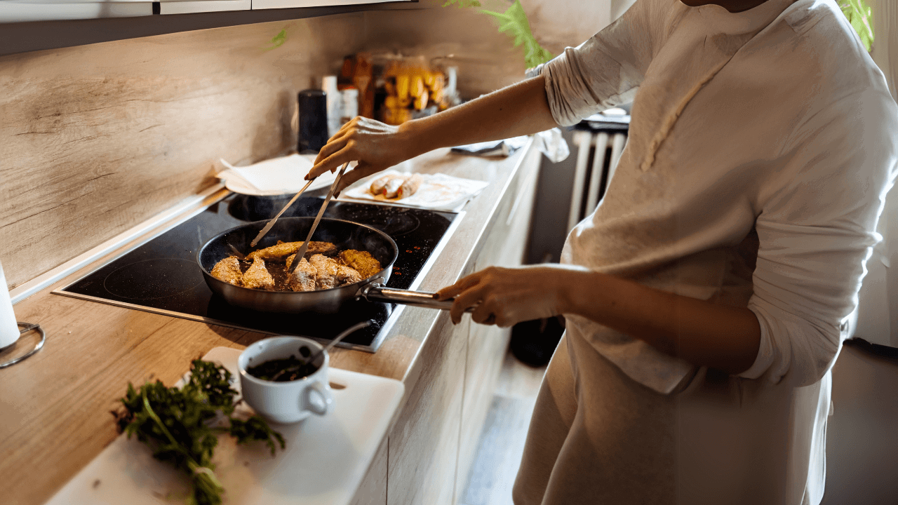 Main Image: A person pan-frying basa fish fillets on the hob, with herbs and cooking accessories on the kitchen counter.