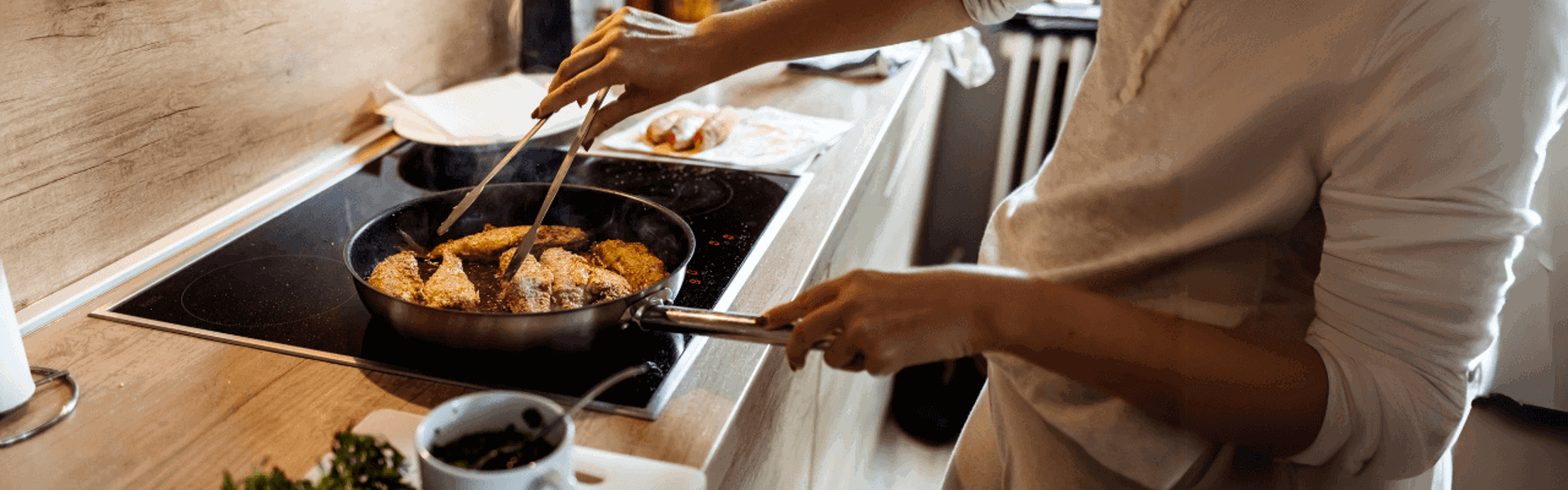 Main Image: A person pan-frying basa fish fillets on the hob, with herbs and cooking accessories on the kitchen counter.