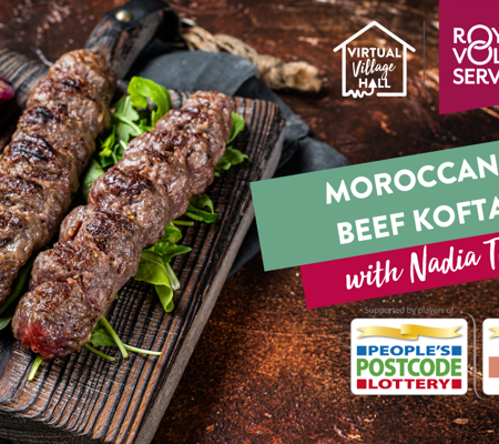 Two grilled meat koftas on wooden board with tomatoes and herbs