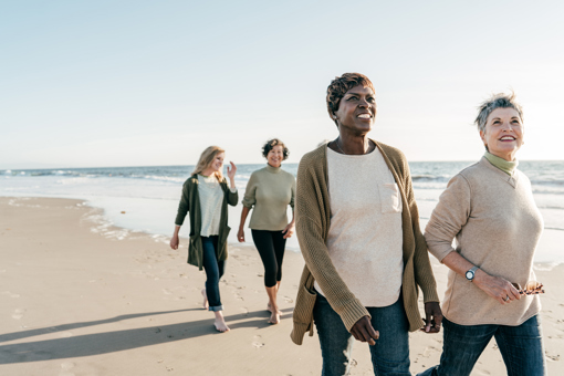 Main image: group of middle aged women walking on the beach, talking and smiling.