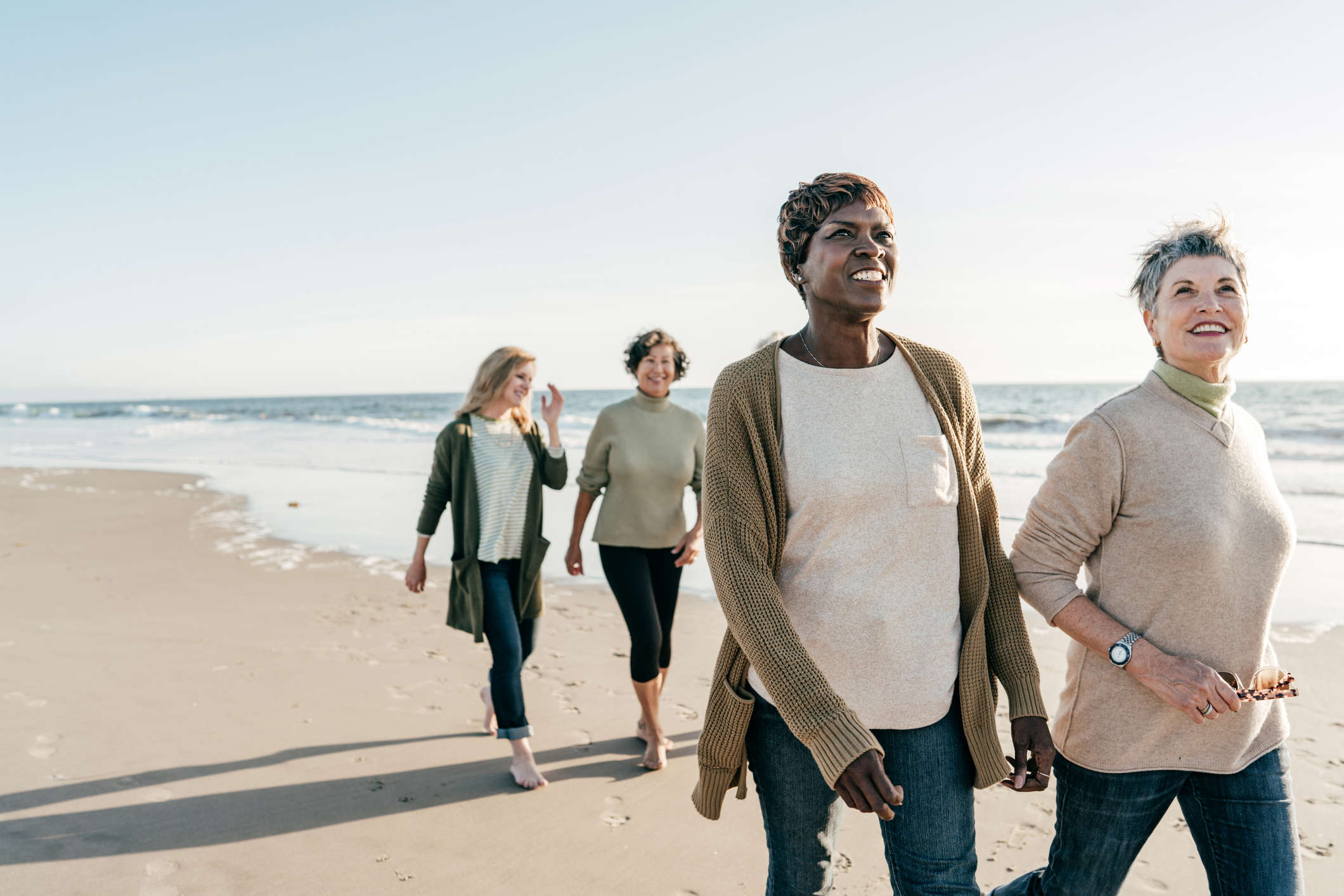 Main image: group of middle aged women walking on the beach, talking and smiling.
