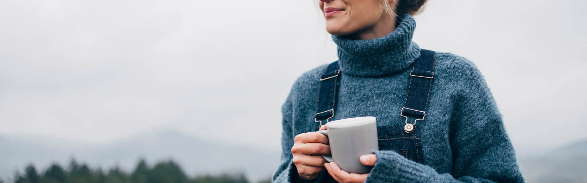 a woman holding a mug of tea outdoors and smiling