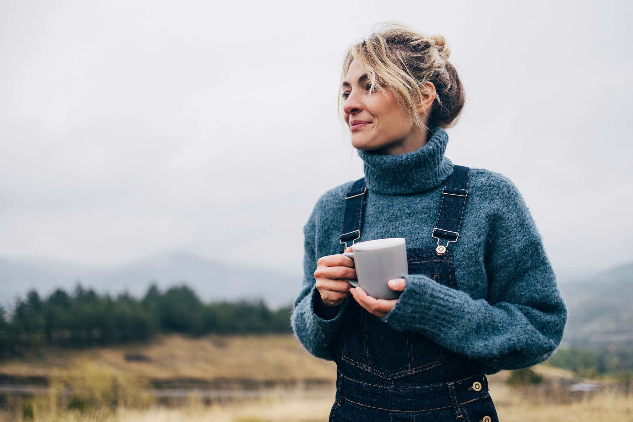 a woman holding a mug of tea outdoors and smiling