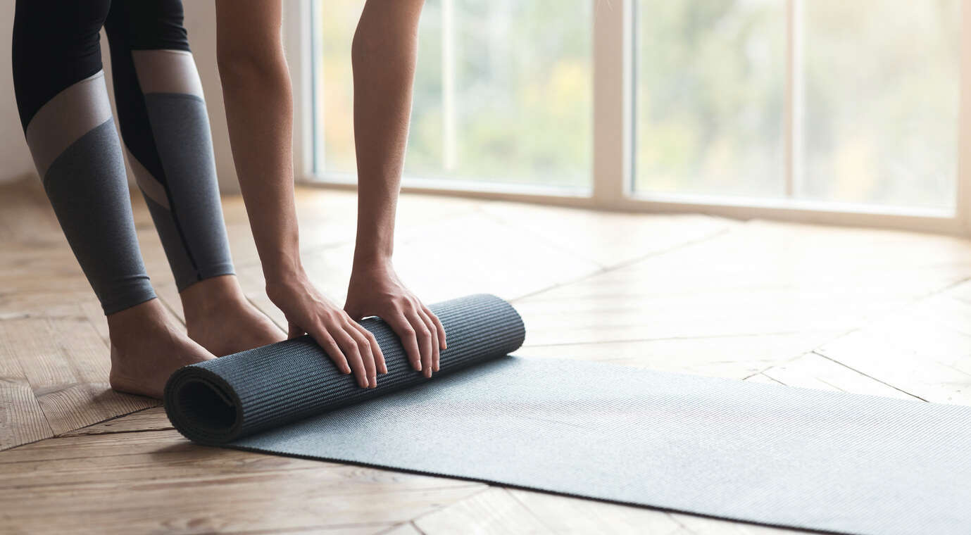 a person rolling up a grey Pilates exercise mat