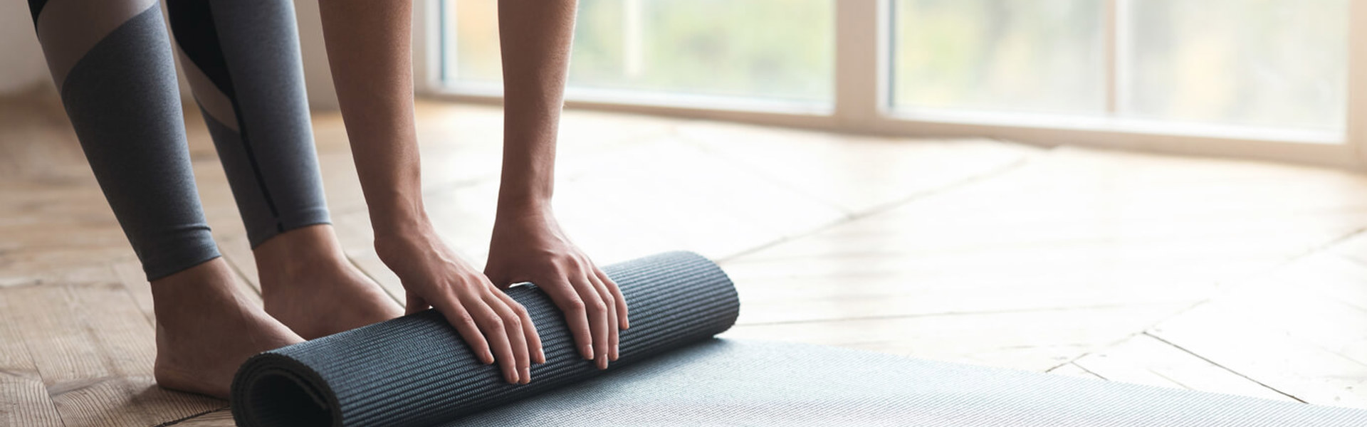 a person rolling up a grey Pilates exercise mat