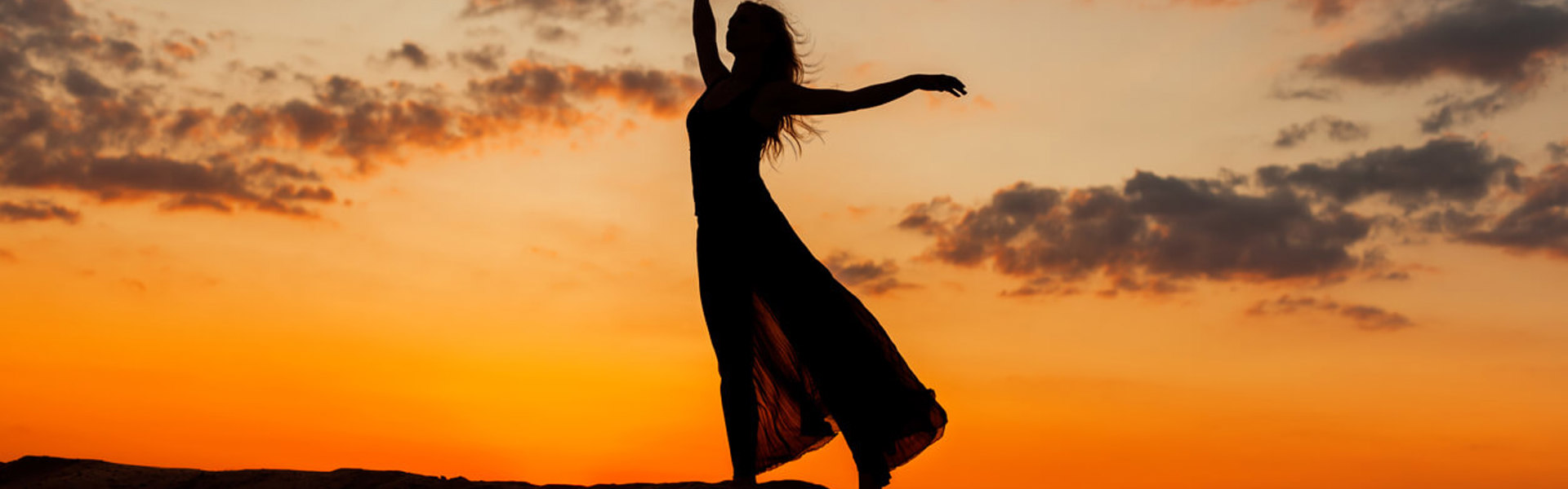 a silhouette of a woman with long hair dancing on a orange horizon in a skirt