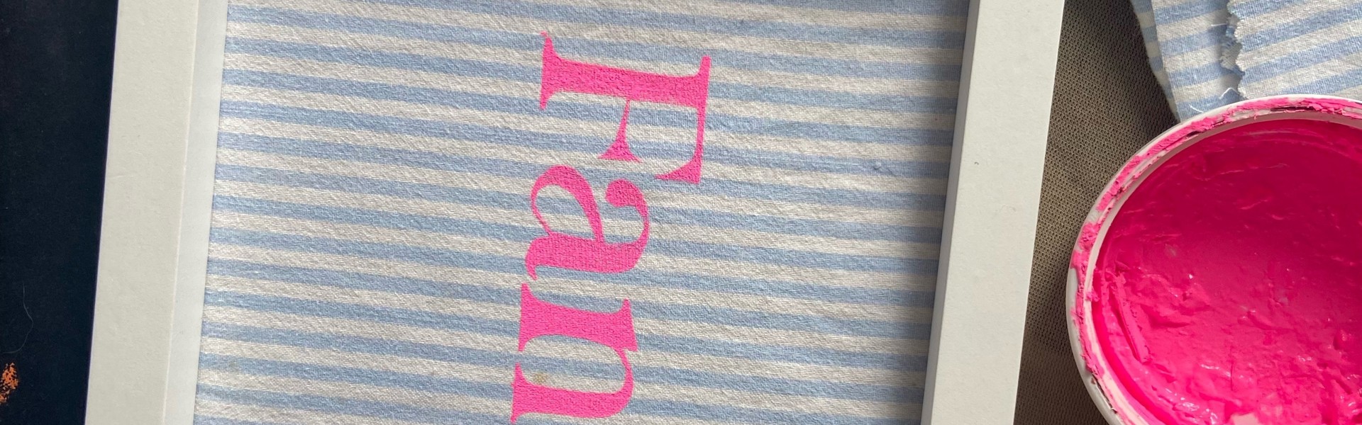 a striped screen print work with neon pink text printed onto it and framed in a white frame
