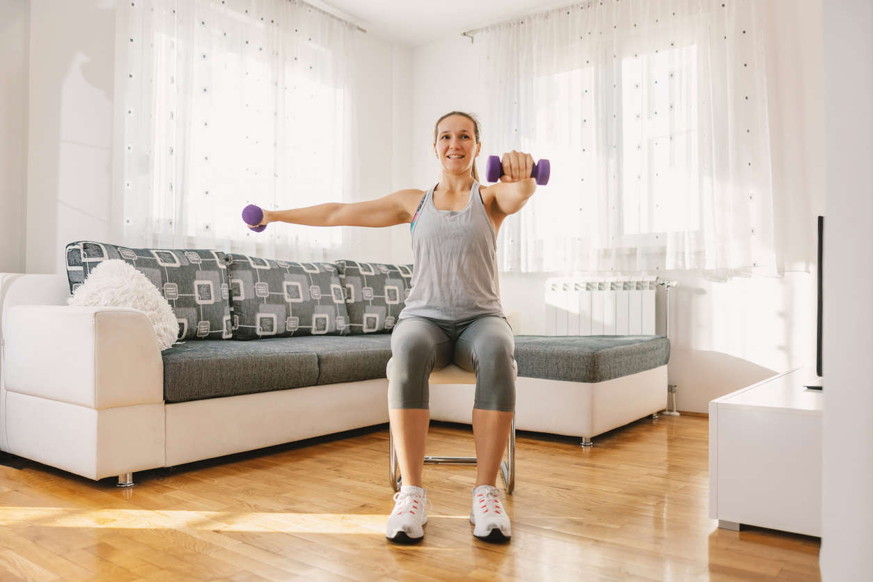 A woman sat on a chair doing exercise with hand weights in the living room