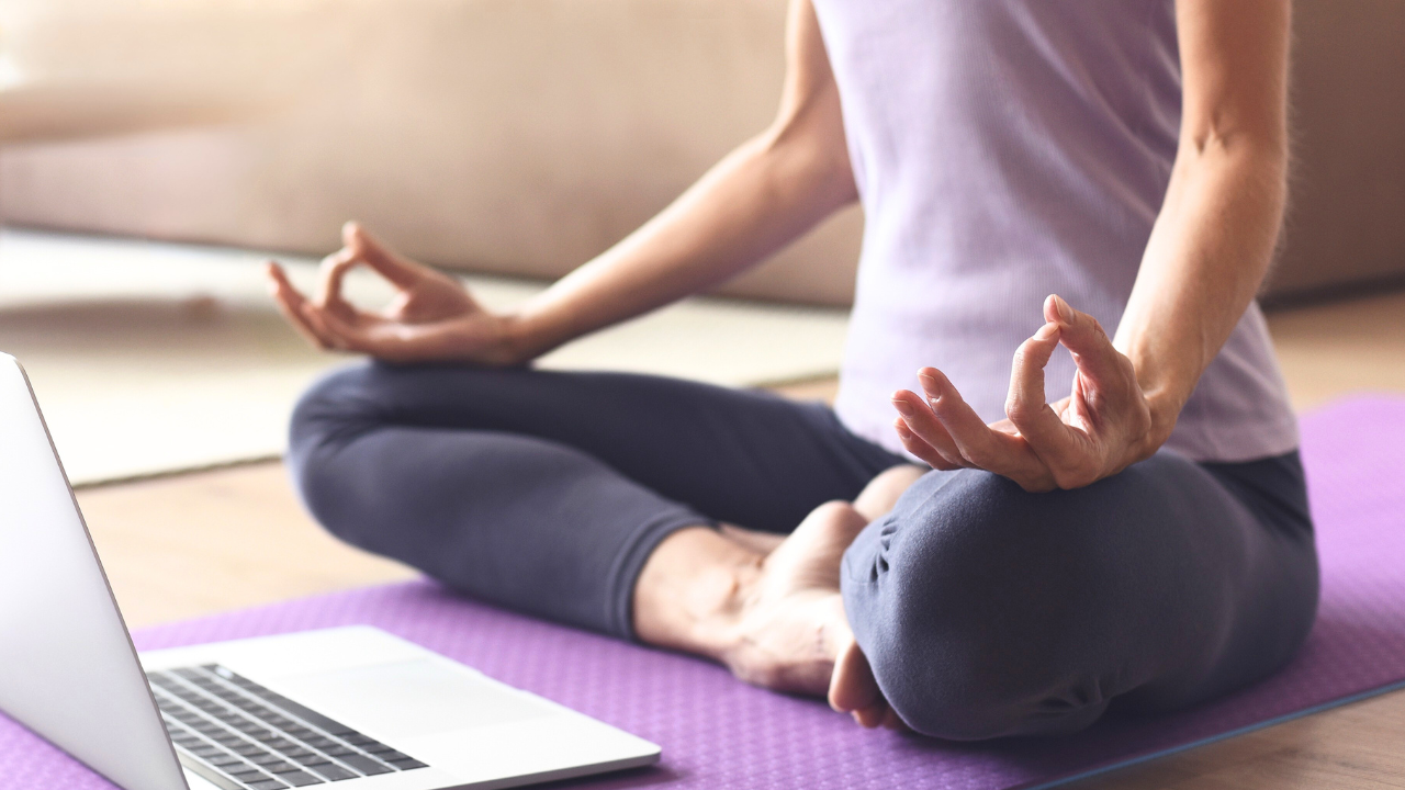 Main Image: a person sat cross legged watching a yoga tutorial from their laptop in the living room