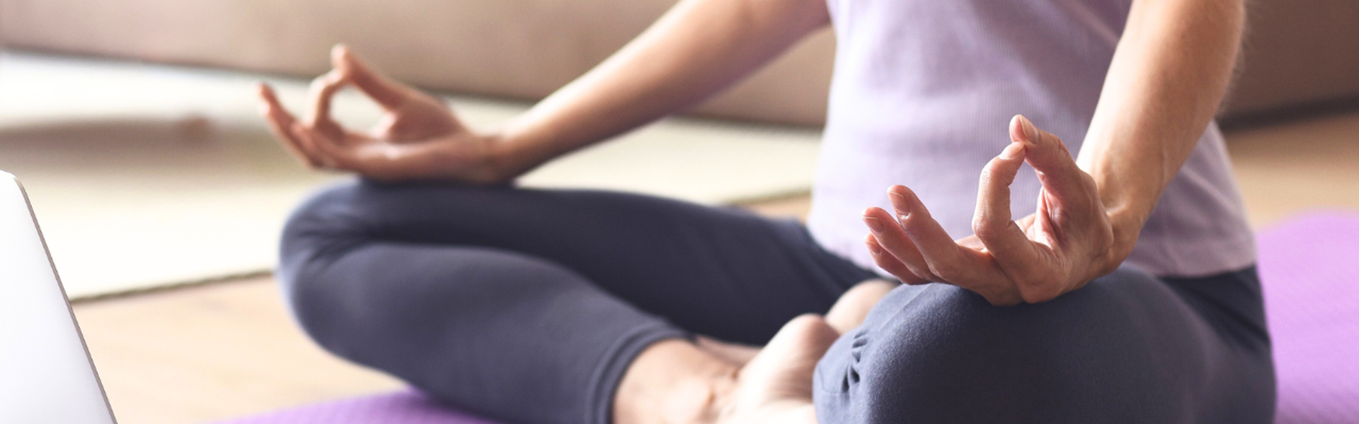 Main Image: a person sat cross legged watching a yoga tutorial from their laptop in the living room