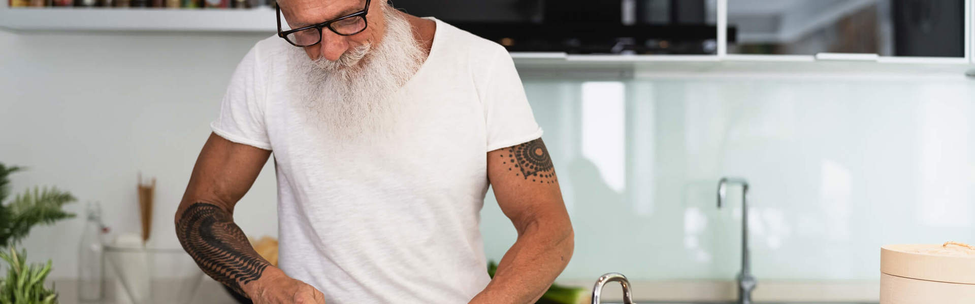 a man with a beard and glasses in a white t-shirt slicing courgette in a kitchen