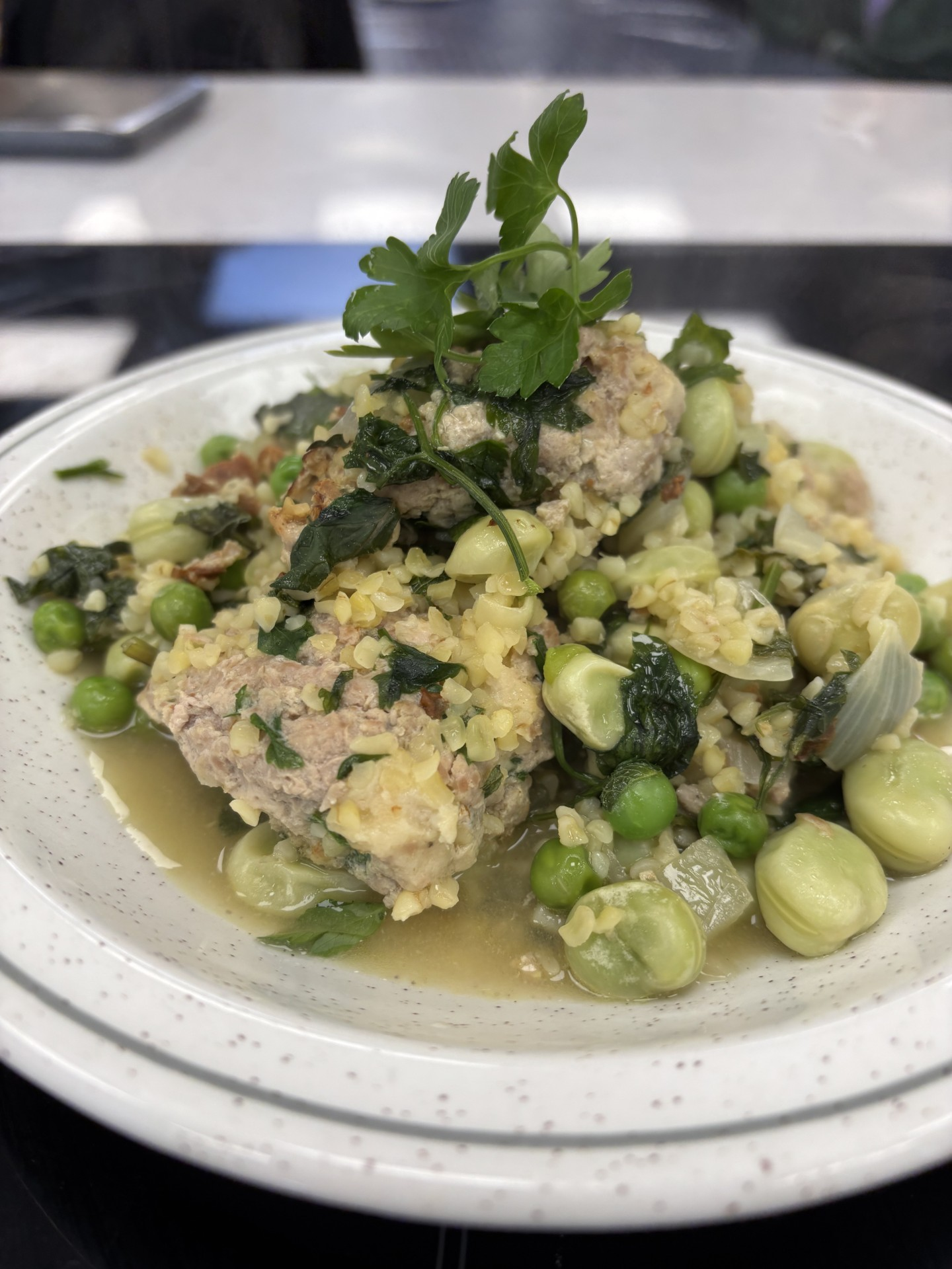 Main Image: Healthy Turkey Meatballs With Bulghur Wheat And Broad Beans on a white plate, with a sprig of parsley on the top.