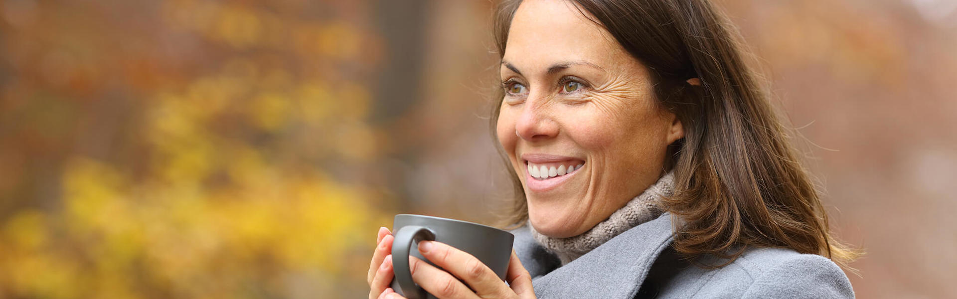 A smiling woman drinking a hot drink outside 