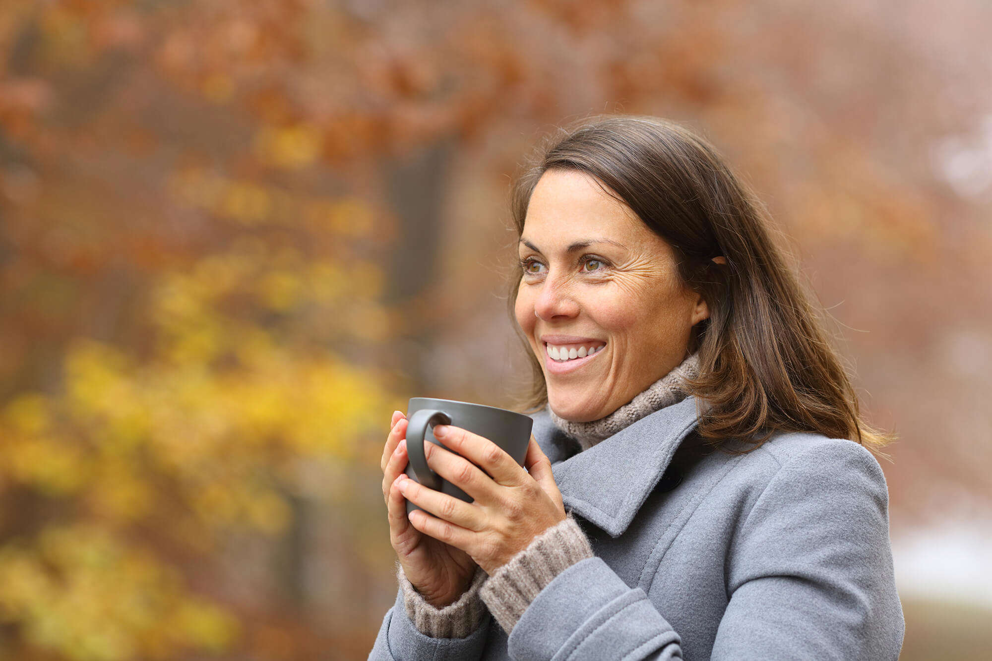 A smiling woman drinking a hot drink outside