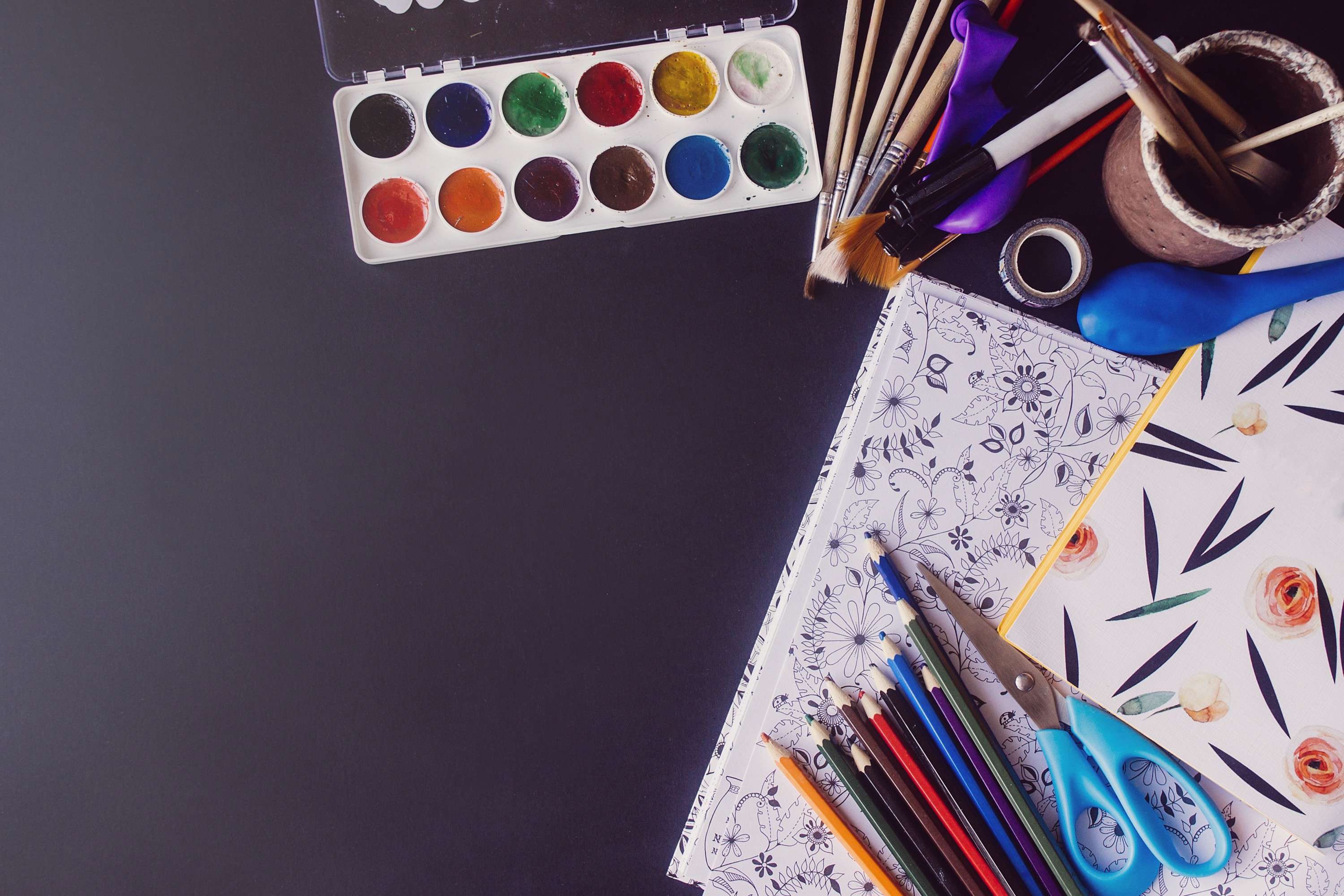 Colouring book, scrap paper, scissors, paint brushes, coloured pencils lay on a black table, ready for a fun and creative art ideas using word prompts session.