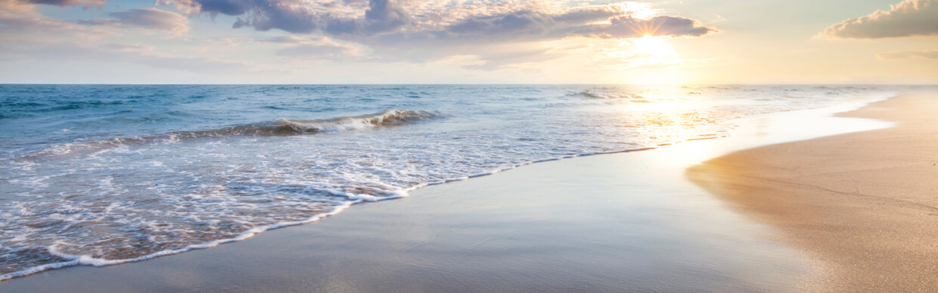 a landscape picture of waves on a sandy beach with a sunset in the background