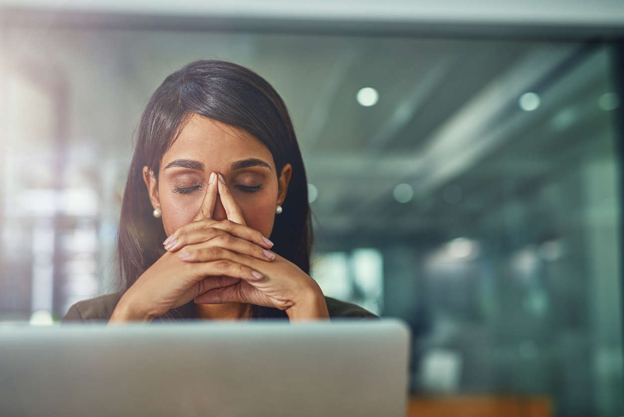 a woman sat at her work desk with her face in her hands experiencing pain