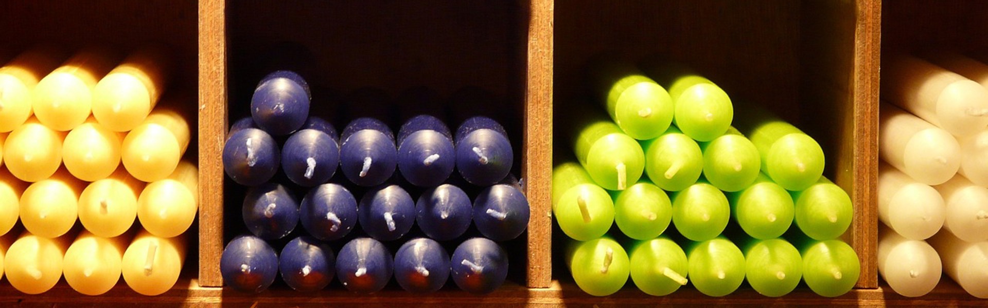 an assortment of coloured candles stacked on wooden shelves