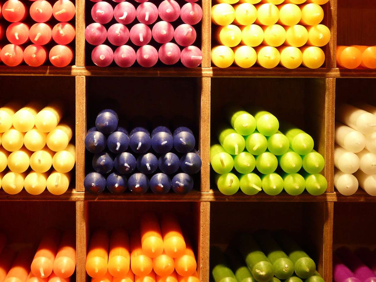 an assortment of coloured candles stacked on wooden shelves